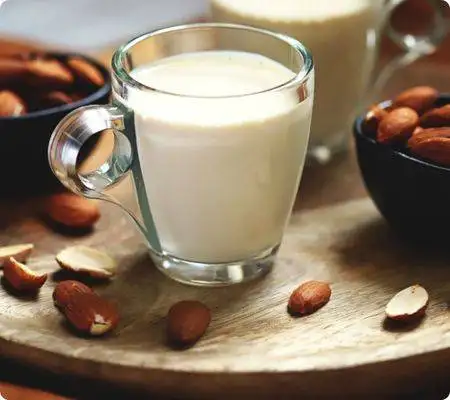 Water or milk for protein shakes. 2 A glass of almond milk on a wooden plate with two small bowls of almond seeds beside it and a few split almond seeds on the wooden plate