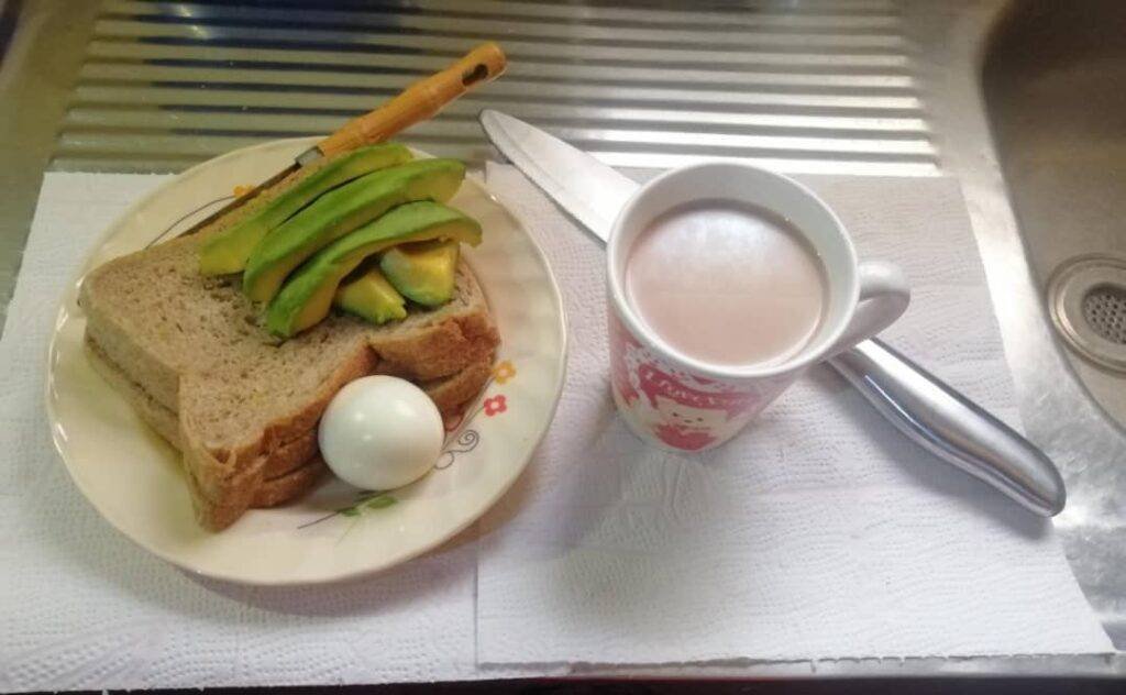 A meal with avocado, boiled egg, and a few slices of bread placed in a flat plate, plus a cup of vitamin rich tea.